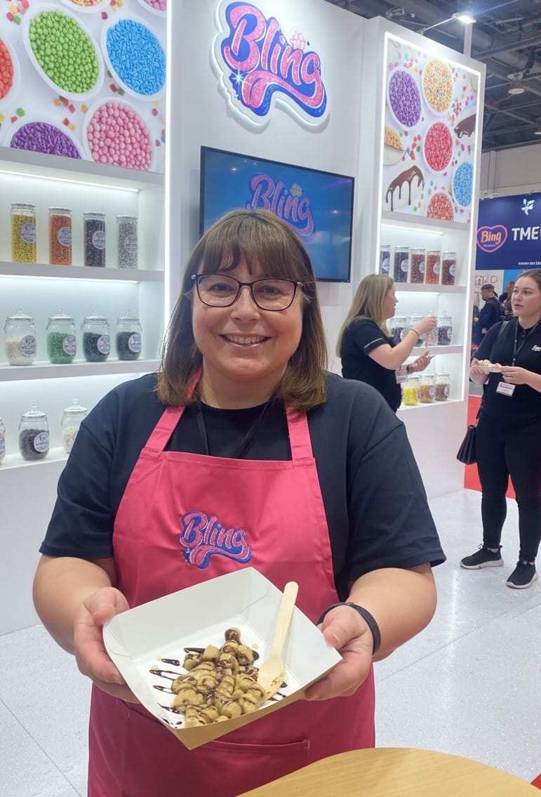 Lady holding warm cookie dough with decorations for food behind her